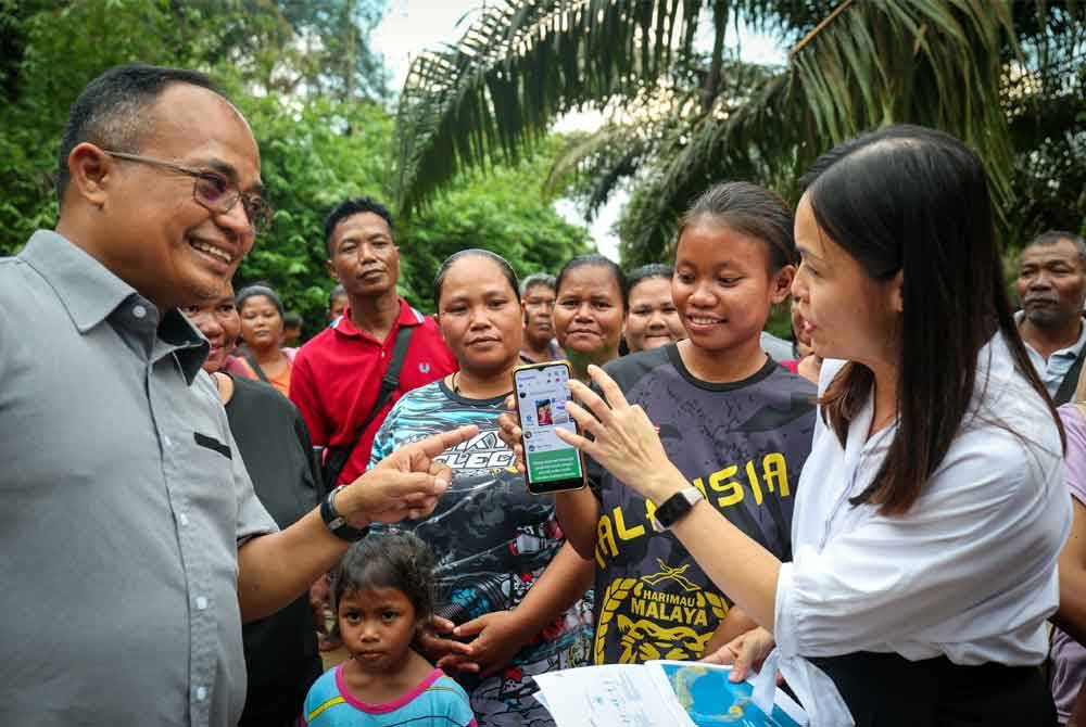 Nie Ching (kanan) melihat telefon pintar milik penduduk kampung yang telah mendapat sambungan internet. Foto Bernama