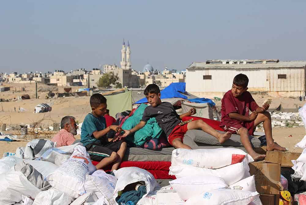 Kanak-kanak Palestin memakan roti di samping barang-barang yang sudah siap dikemas sebelum berpindah ke Rafah di Gaza. Foto AFP