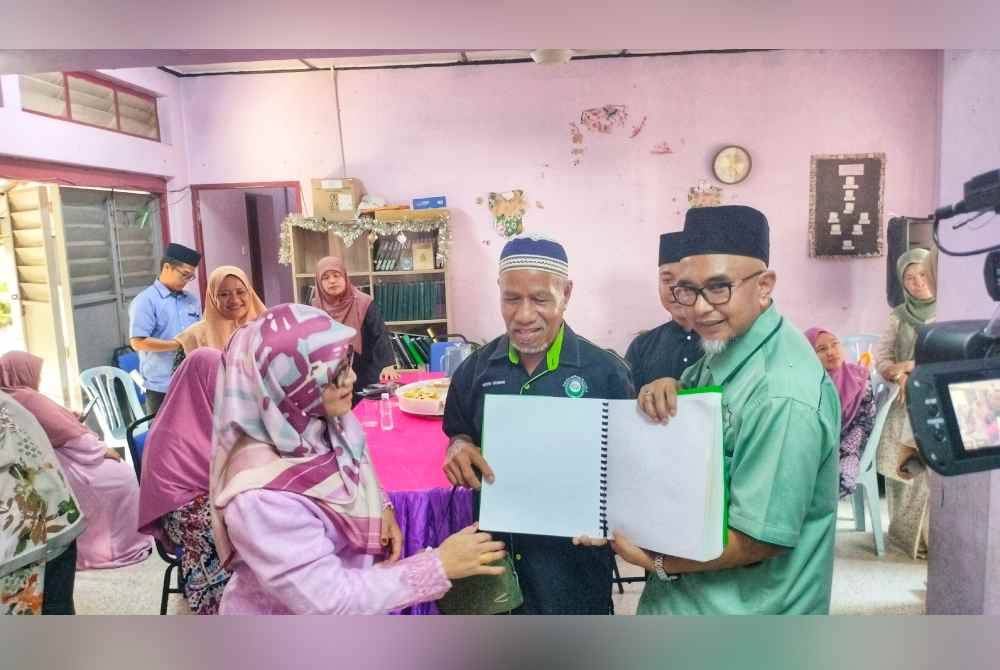 Sabariah (kiri) melihat al-Quran braille yang digunakan oleh persatuan itu oleh Mohd Bakhri (tengah) sambil diperhatikan Mohd Zawawi (kanan).