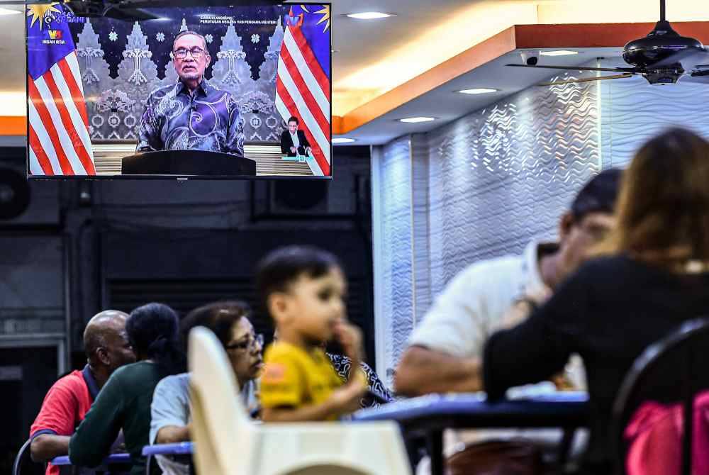 Orang ramai menyaksikan Perutusan Negara oleh Perdana Menteri yang disiarkan secara langsung melalui televisyen ketika tinjauan di sebuah restoran sekitar ibu kota malam ini. Foto Bernama