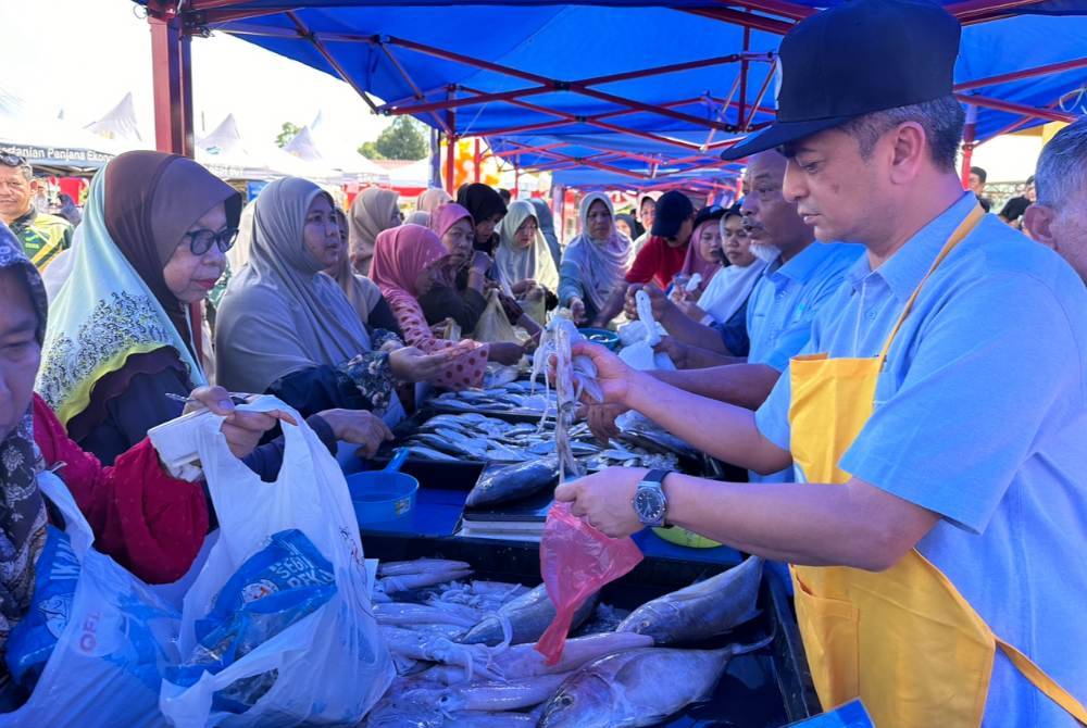 Muhammad Faiz (kanan) melayani orang ramai yang membeli makanan basah di Pasar Nelayan Pulau Gajah, Kota Bharu pada Sabtu.