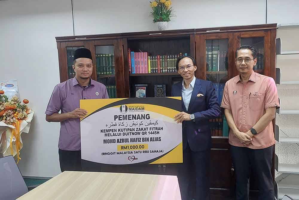 Ahmad Azrin (tengah) menyerahkan mock cheque berjumlah RM1,000 kepada pemenang Kempen kutipan zakat fitrah melalui pembayaran DuitNow QR, Mohd Azrul Hafiz (kiri).