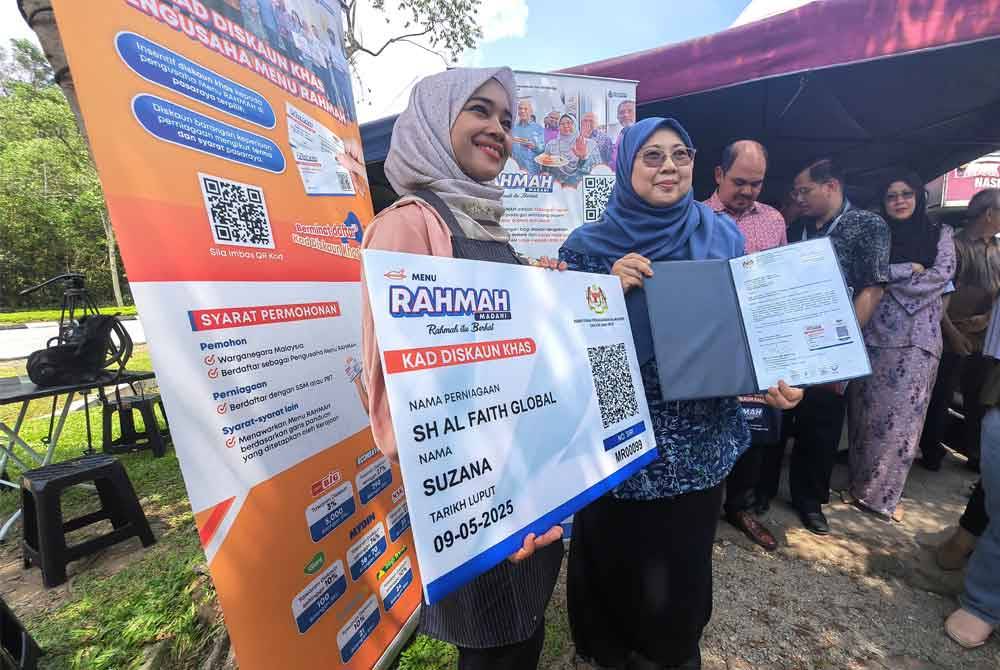 Fuziah menyerahkan replika Kad Diskaun Khas Menu Rahmah kepada seorang peniaga di Taman Desa Anggerik di Nilai.