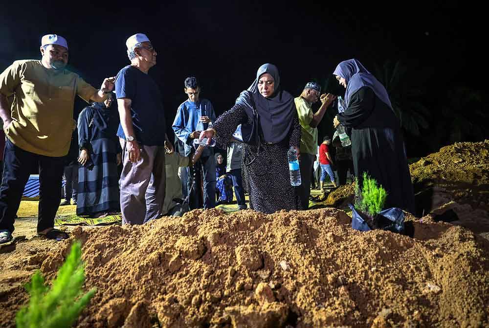 Nur-ul Afida menyiram air di pusara selepas pengebumian jenazah abangnya. Foto Bernama