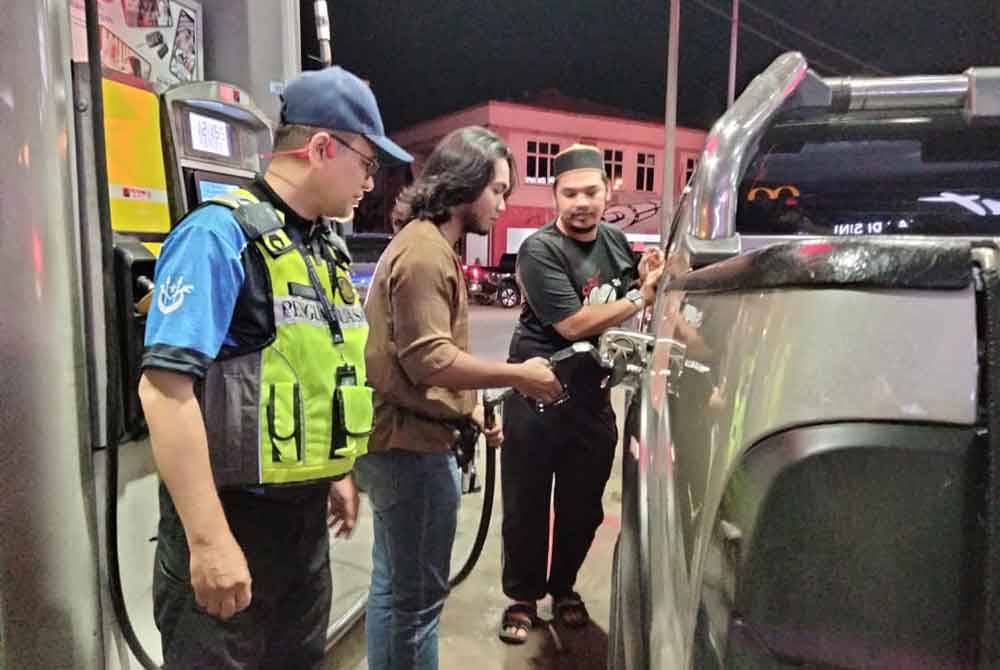 Azman (kiri) melihat pengguna mengisi petrol di stesen minyak Petron di Pasir Pekan pada Ahad.