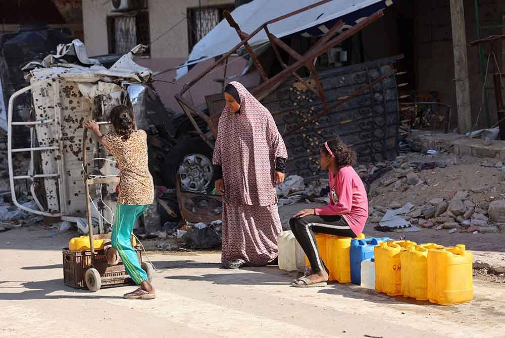 Wanita dan kanak-kanak Pelastin mengambil air melalui kawasan bangunan yang musnah dibom Israel di bandar Gaza pada Isnin. Foto AFP