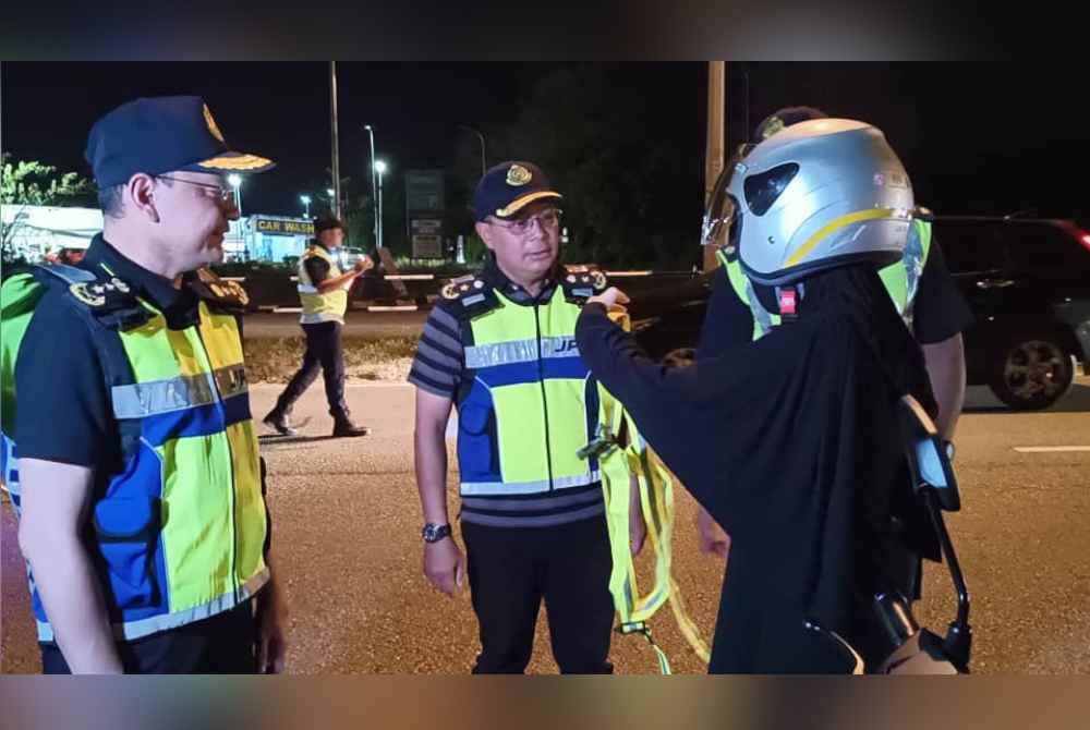 Stien (kiri) menyoal seorang penungang motosikal yang diperiksa di hadapan pejabat JPJ Sungai Petani pada malam Khamis.