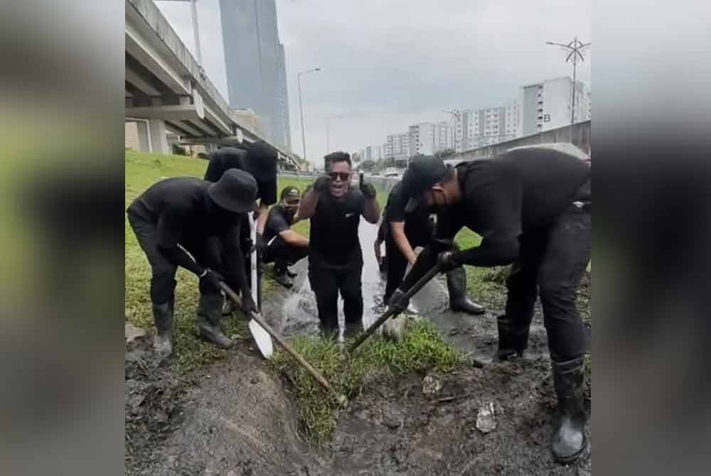 Kumpulan pemuda berbaju hitam bergotong-royong membersihkan longkang yang tersumbat di tepi jalan berhadapan sebuah pusat membeli-belah.