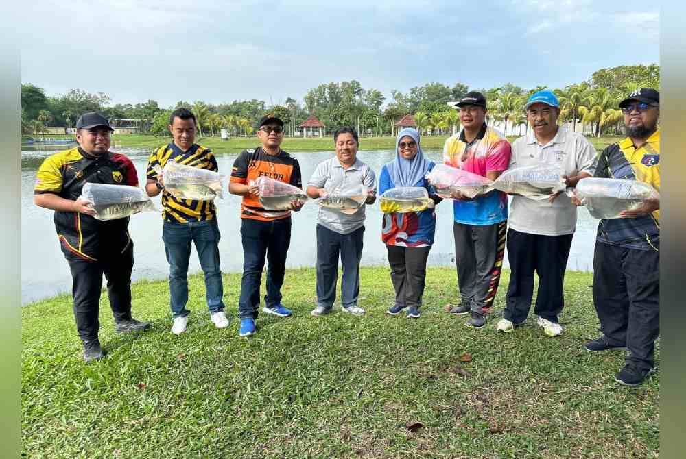 Razuwan (tiga dari kiri) dan Mohd Shaidee (empat dari kiri) menunjukkan spesies patin buah yang dilepaskan ke Tasik Maeps.