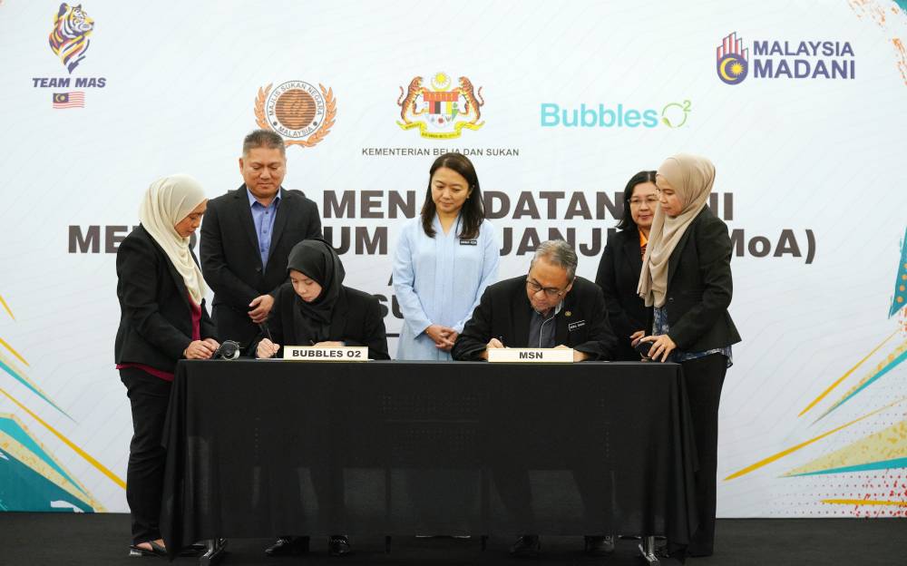 Ain Azizah bersama Abdul Rashid menandatangani memorandum perjanjian persefahaman disaksikan oleh Hannah Yeoh (tengah) dan Arifin (berdiri, dua dari kiri) pada majlis Menandatangani Memorandum Perjanjian (MoA) antara Majlis Sukan Negara dan Bubbles O2 Sdn. Bhd di sini pada Selasa.