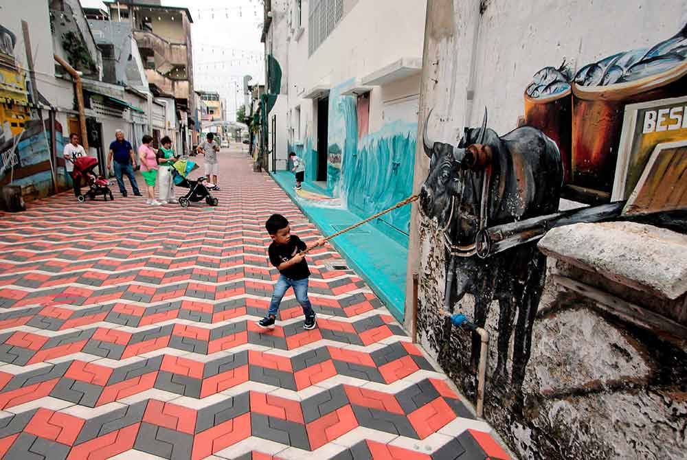 Gelagat pengunjung cilik, Rayyan Al Fateh Amizee, 4, "menarik" seekor kerbau yang menjadi salah satu lukisan mural di Kuantan Art Street hari ini.