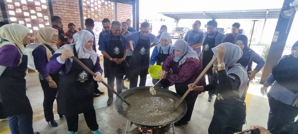 Rubiah (dua dari kanan) turut sama membantu memasukkan bahan-bahan untuk memasak bubur asyura.