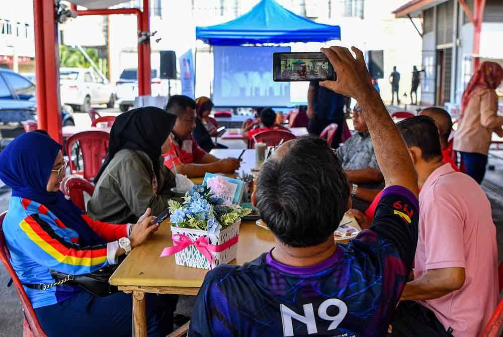 Seorang pelanggan dilihat merakam momen bersejarah ketika menyaksikan layar pacak yang disediakan oleh Jabatan Penerangan Negeri Sembilan semasa menyaksikan Istiadat Pertabalan Yang di-Pertuan Agong ke-17 yang berlangsung di Istana Negara ketika tinjauan di Pasir Panjang pada Sabtu. Foto Bernama