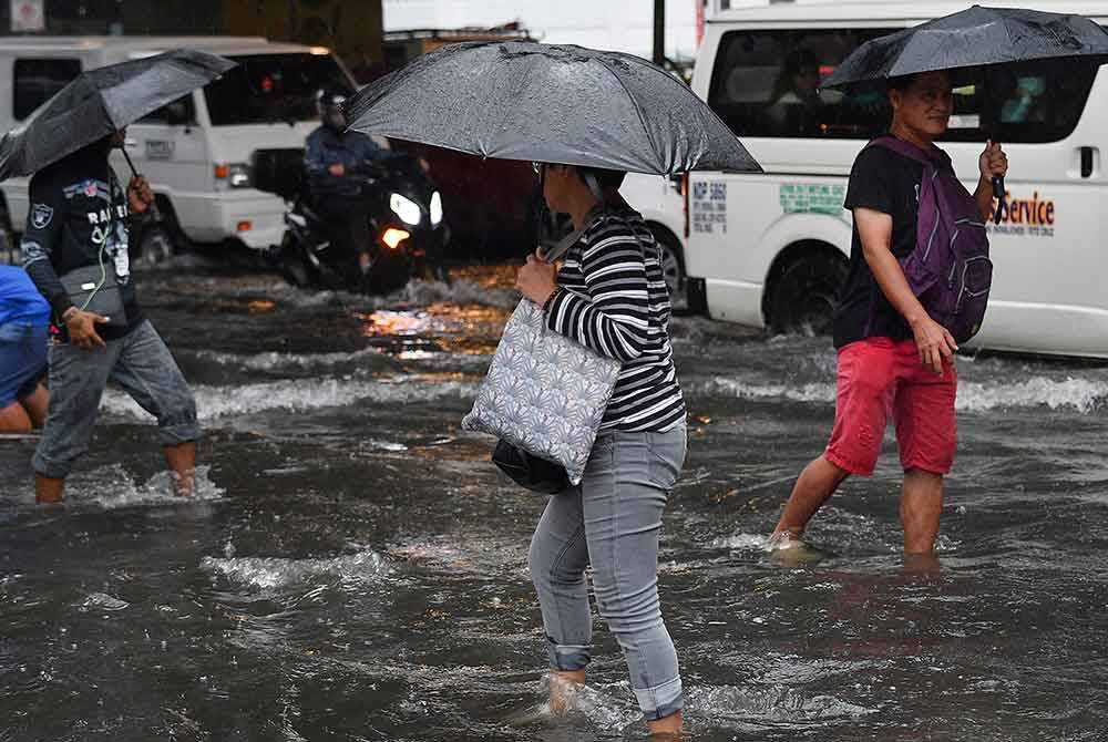 Pejalan kaki mengharungi jalan yang dinaiki air di Manila pada Selasa di tengah-tengah hujan lebat yang dibawa oleh Taufan Gaemi. - Foto: AFP