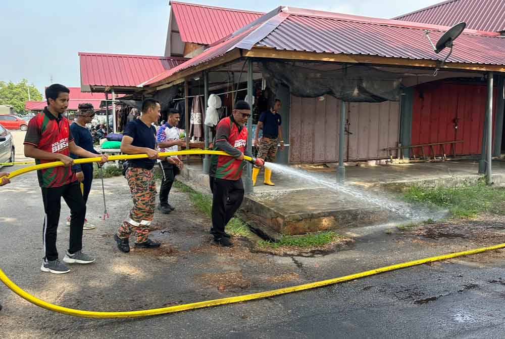 Muhammad Zuhairi (kiri) dan Zubir (dua dari kanan) dan anggota bomba mencuci longkang di kawasan Pasar Borong Sri Guchil, Kuala Krai.