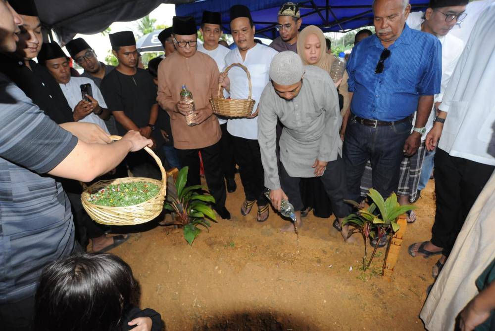 Wan Mohd Hibatullah (tengah) menyiram air di pusara ibunya di Tanah Perkuburan Islam Raudathus Sakinah Kampung Tengah, Kluang, pada Jumaat.