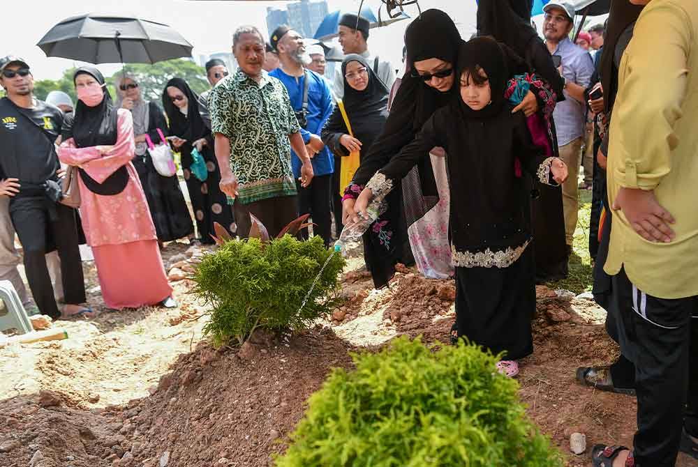 Anak Allahyarham Mohd Fauzi Darus atau dikenali sebagai Jay Jay, Nur Camelia Mohd Fauzi bersama anaknya menyiram air bunga mawar di atas pusara bapanya di Tanah Perkuburan Bukit Tandang, pada Isnin. Foto Bernama