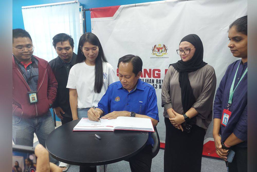 Ahmad (duduk) menandatangani buku pelawat ketika meninjau Pusat Media Rasmi PRK Nenggiri di Dataran Kesedar, Kampung Sungai Asap, Gua Musang pada Selasa.