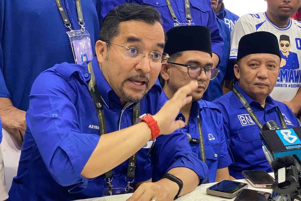 Asyraf Wajdi (kiri) semasa sidang akhbar selepas pengumuman kemenangan calon BN, Mohd Azmawi Fikri (tengah) di Dewan Perdana, Kompleks Perdana, Majlis Daerah Gua Musang pada Sabtu.