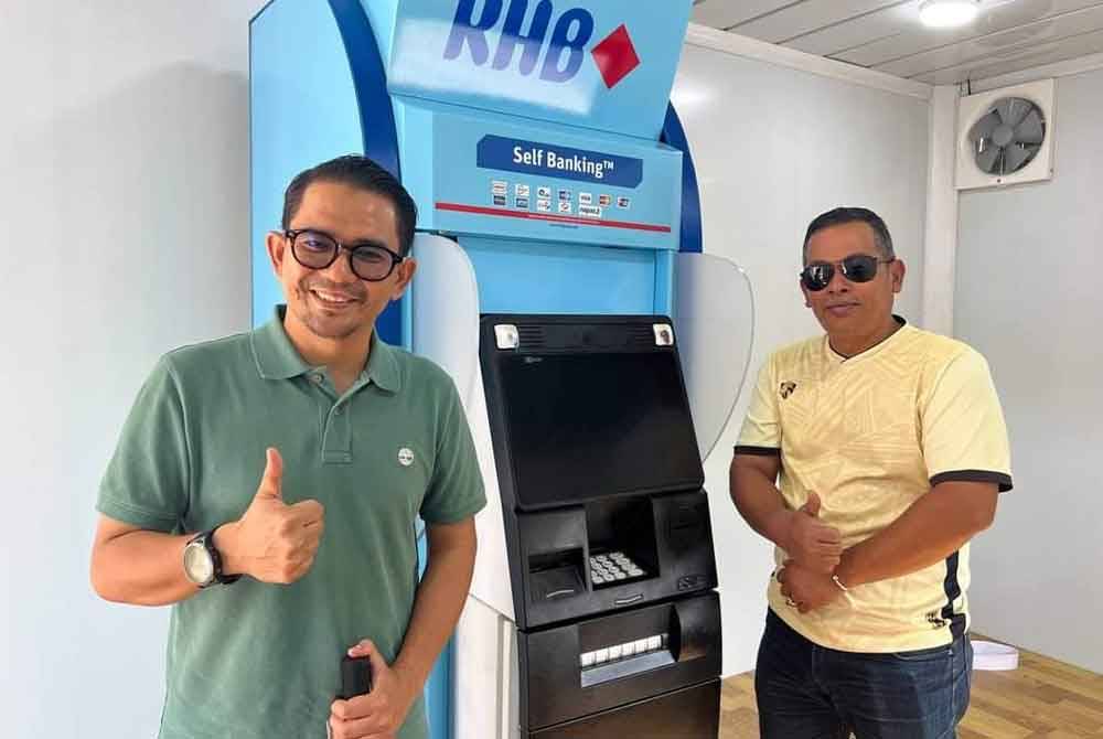 Awie (kiri) menunjukkan mesin ATM kedua yang dipasang untuk penduduk di DUN Nenggiri.