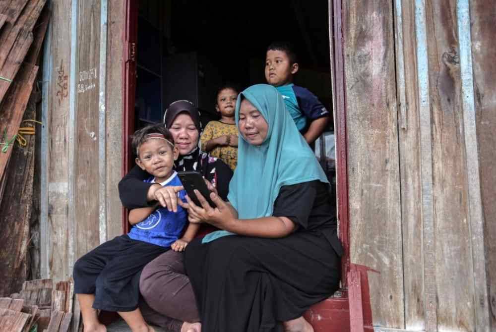 Penduduk, S Roha, 40, (kanan) dan Nurjina, 42, (dua, kiri) bersama meluangkan masa menggunakan telefon bimbit di Kampung Sungai Tonggang ketika ditemui baru-baru ini. Foto Bernama