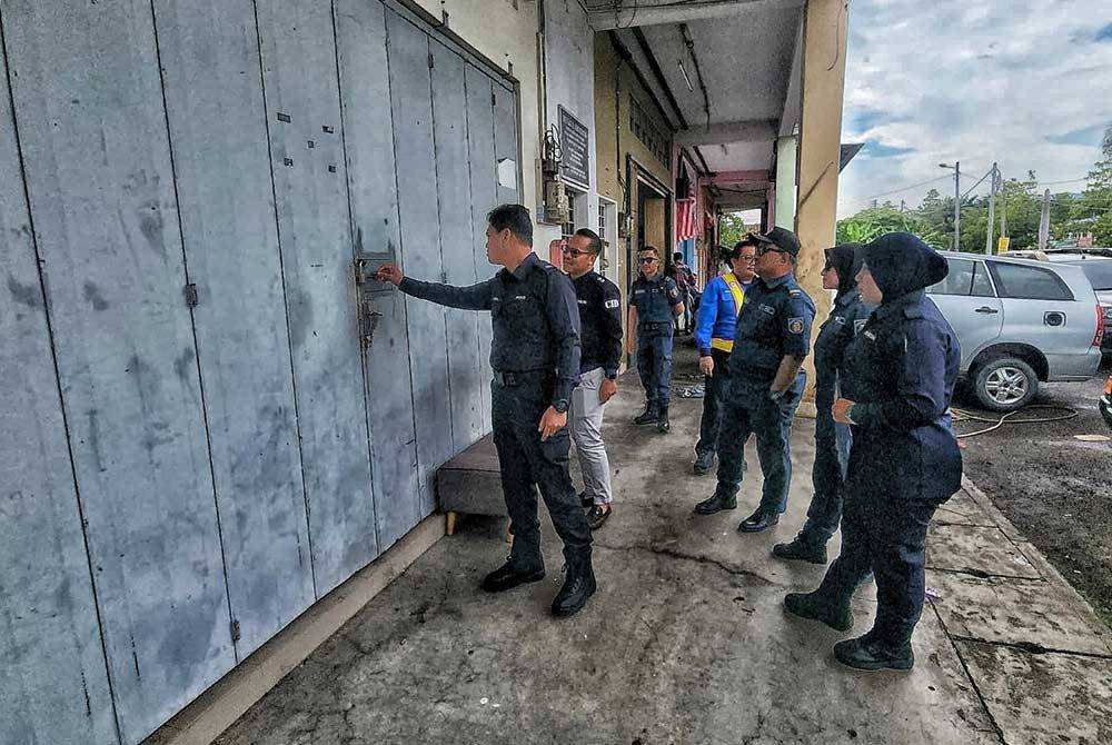 Azrul (kiri) melihat lubang kecil yang terdapat di pintu sebuah premis yang dipercayai menjalankan aktiviti perjudian di Taman Samarinda pada Khamis.