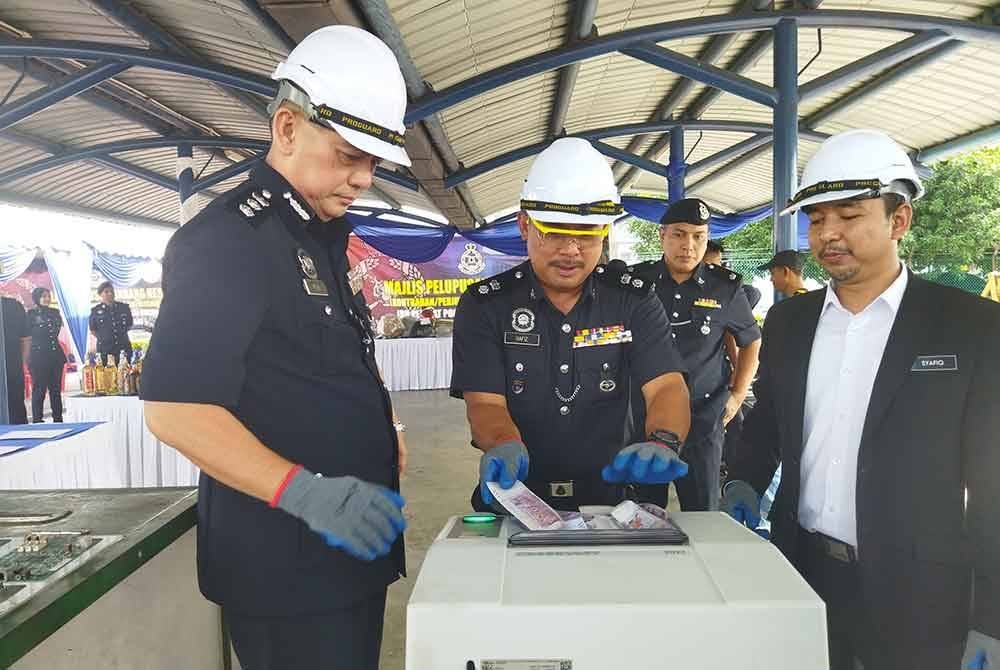 Mohd Hafiz (tengah) melupuskan wang palsu di IPD Sungai Buloh, di sini, pada Jumaat.