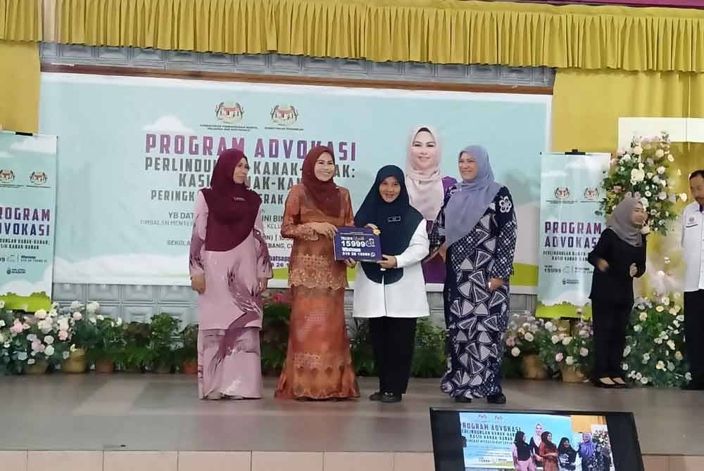 Noraini (dua dari kiri) menyerahkan pelekat khas kepada wakil sekolah-sekolah di Perak sempena Program Advokasi Perlindungan Kanak-Kanak: Kasih Kanak-Kanak Peringkat Negeri Perak di Sekolah Kebangsaan Seri Kelebang, Chemor di sini, pada Isnin.