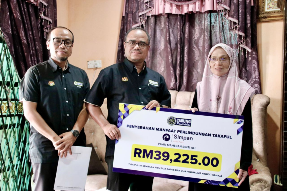 Mohd Rusdi (tengah) menyerahkan replika kad manfaat perlindungan takaful Simpan SSPN Plus kepada Maheran (kanan) diiringi Fauzi Azli di Kampung Genting Palas, Kuala Nerang, pada Ahad.