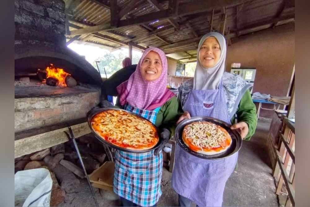 Nur Faizah (kiri) bersama madunya, Sarinah menunjukkan pizza yang sedia untuk dimasak dan dihidangkan kepada pelanggan ketika ditemui di Warung Seni Bidadara Pizza dekat Kampung Lubuk Kawah, Besut.