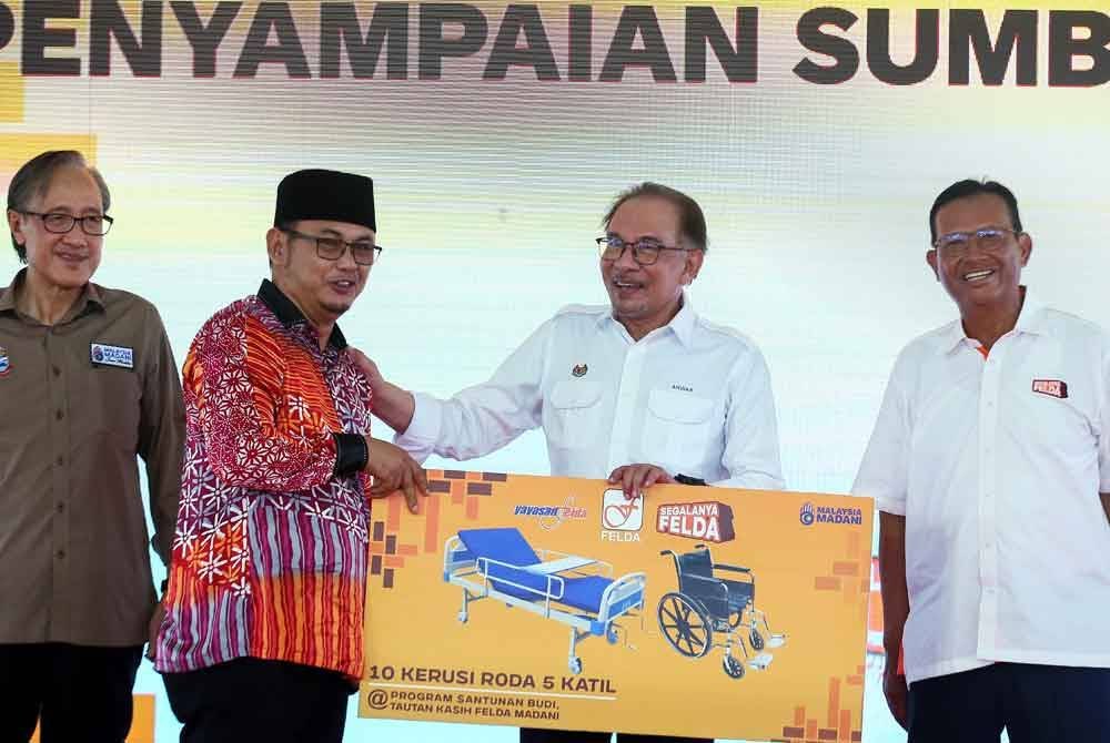 Anwar (dua, kanan) menyampaikan sumbangan katil dan kerusi roda dari Yayasan Felda kepada wakil Komuniti Felda Gugusan Sahabat, Sharif Musa (dua, kiri) selepas merasmikan Majlis Santunan Budi Tautan Kasih Felda Madani di Padang Bandar Felda Sahabat pada Khamis. Foto Bernama