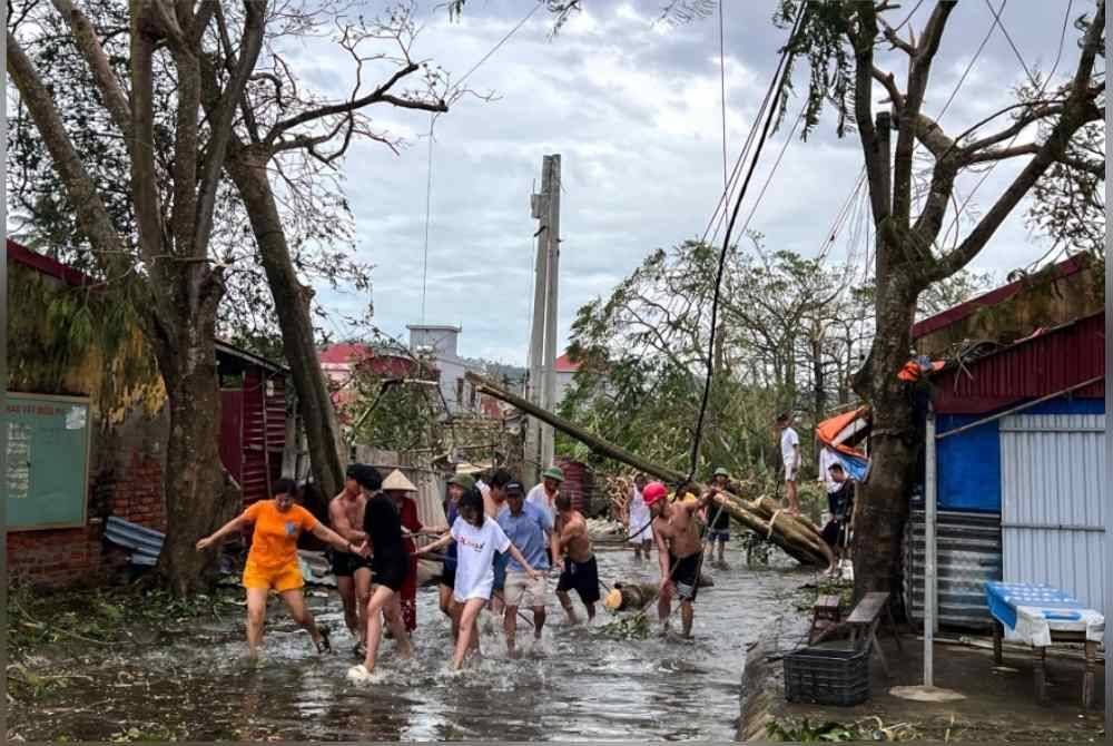 Orang ramai menggunakan tali untuk mengalihkan pokok tumbang berikutan kesan Taufan Yagi, Hai Phong, Vietnam. Foto Reuters