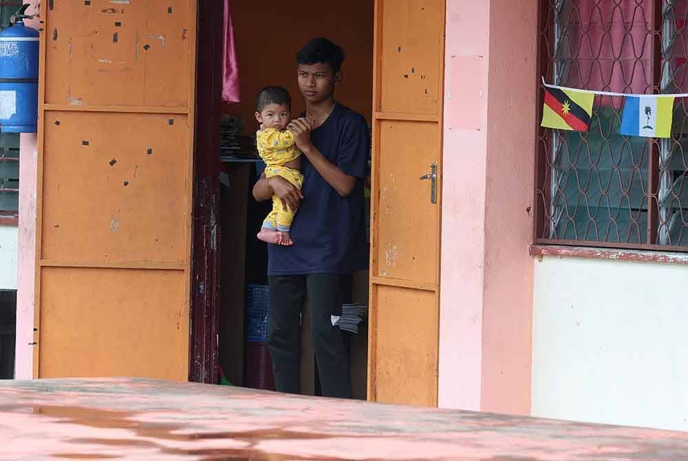 Muhammad Rusmizan Azimi, 15, bersama anak saudaranya, Muhammad Aryan Rizqi Muhammad Alif, 6 bulan, berada di Pusat Pemindahan Banjir di Sekolah Kebangsaan Malau di sini selepas rumah mereka di Kampung Baru, Malau, dinaiki air sejak semalam. Foto Bernama