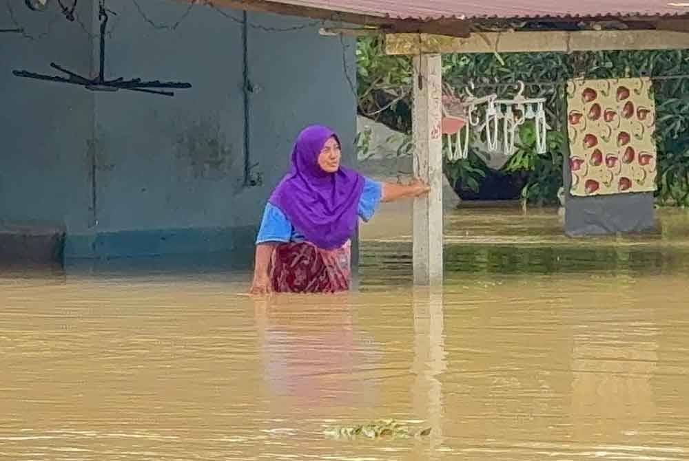 Zaiton meredah banjir di hadapan rumahnya.