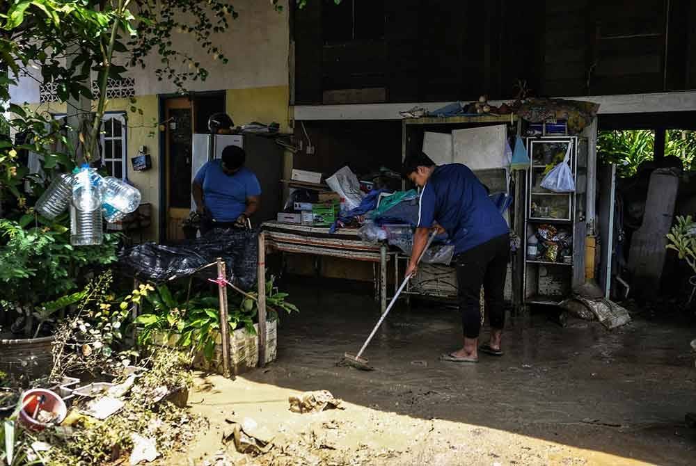 Penduduk mula membersihkan rumah mereka yang dipenuhi lumpur selepas air banjir surut, semasa tinjauan di Kampung Suka Menanti, Alor Setar pada Selasa. Foto Bernama