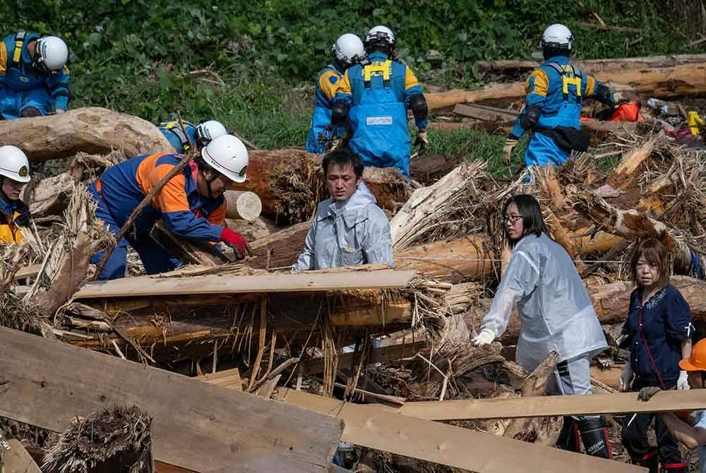 Seorang bapa (tengah) mencari anak perempuannya yang berusia 14 tahun di sebalik sisa kayu yang dibawa banjir di sepanjang sungai Tsukada berikutan hujan lebat di bandar Wajima, wilayah Ishikawa pada 23 September 2024. Foto AFP