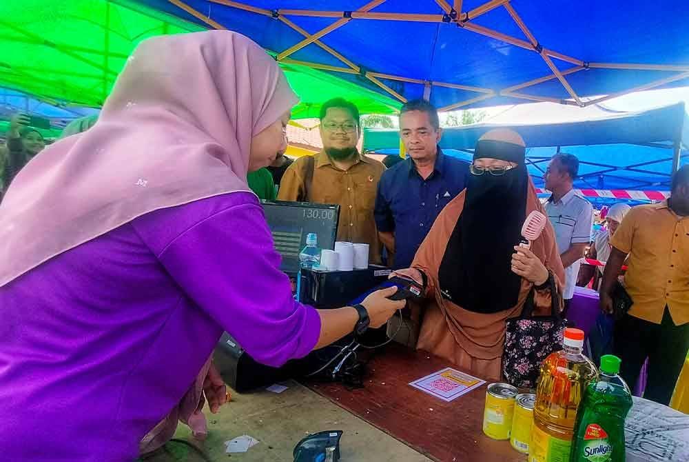 Mohd Faizal (tiga dari kanan) dan Shahrizal (dua dari kanan) melihat urusan transaksi tanpa tunai penduduk sempena program Cashless@NADI Felda Jenderak Utara pada Rabu.