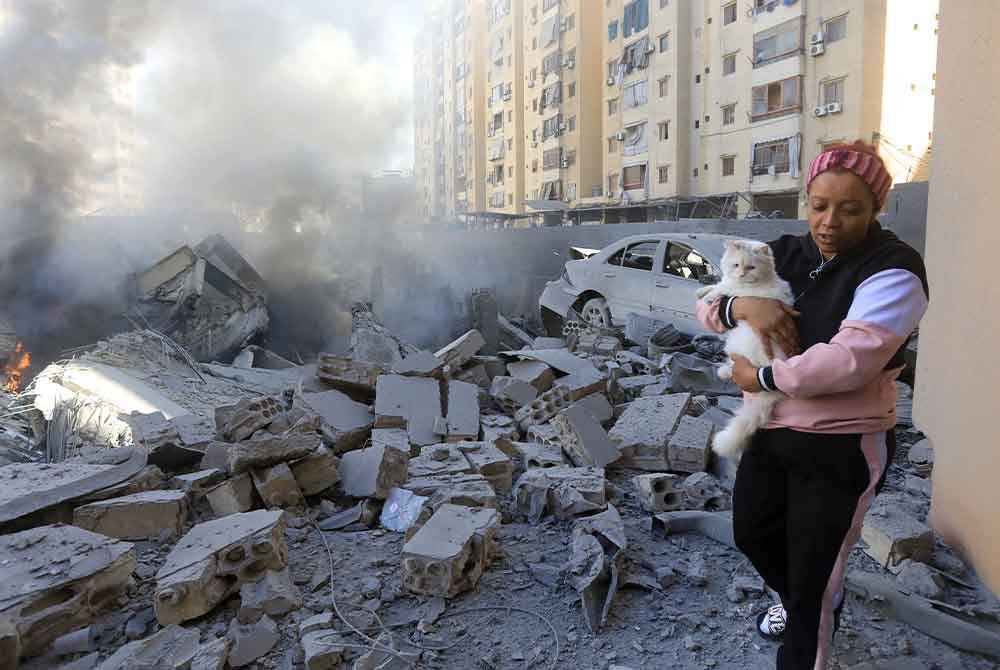 Seorang wanita membawa kucing melepasi bangunan yang musnah di tapak serangan udara Israel semalaman di pinggir bandar Shayyah, selatan Beirut pada Rabu. Foto AFP