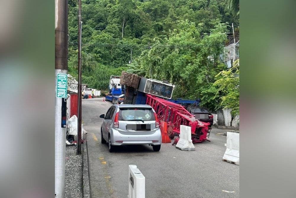 Kren yang dibawa sebuah treler terbalik lalu terkena sebuah rumah dan kereta di kawasan berhampiran. Foto FB Connie