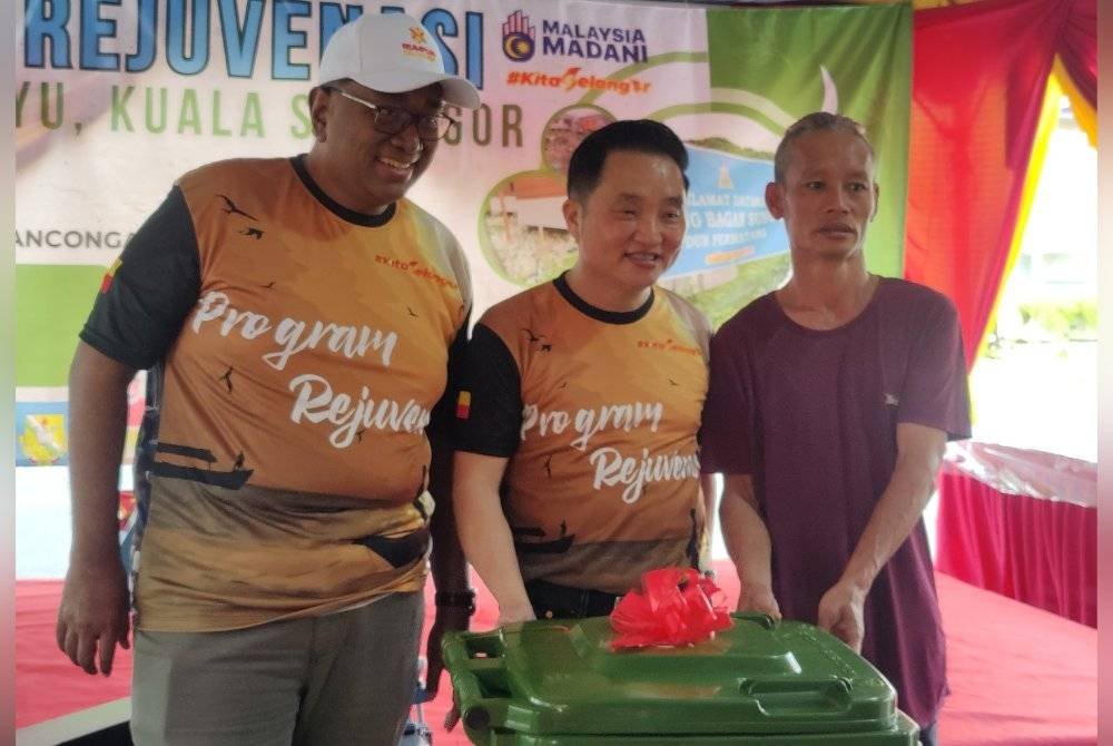 Suee Lim (tengah) diiringi Pegawai Daerah Kuala Selangor, Mohd Raiz Radzuan (kiri) menyerahkan tong sampah kepada salah seorang penduduk semasa Program Rejuvenasi di Kampung Bagan Sungai Yu di sini pada Sabtu.