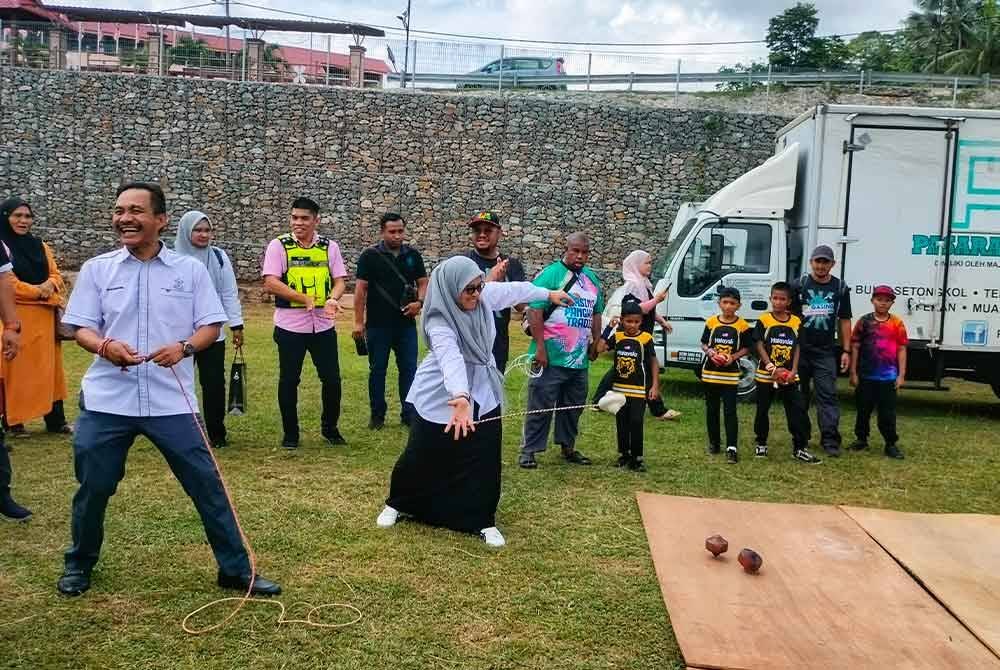 Sabariah (tengah) dan Sharuddin (kiri) tidak melepaskan peluang bermain gasing dalam karnival tersebut.