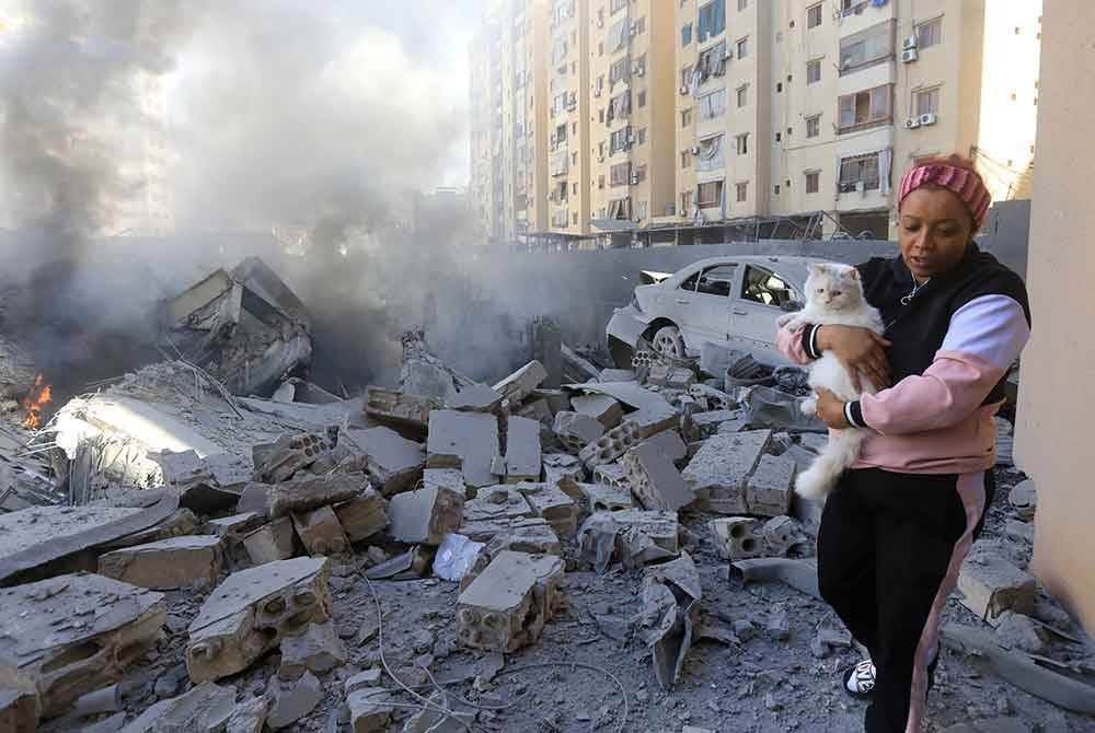 Seorang wanita mengendong kucingnya untuk menyelamatkan diri semasa serangan udara di selatan Beirut. - AFP