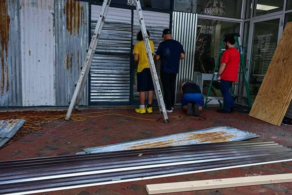 Beberapa pekerja di Kissimmee, Florida memasang pelindung di hadapan pintu kaca di premis perniagaan mereka.