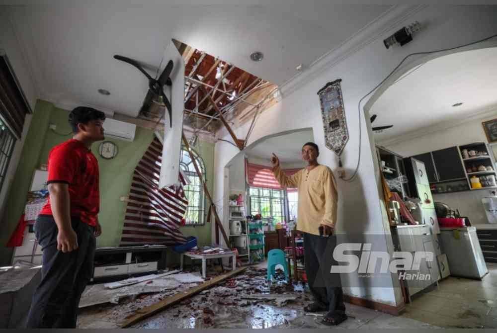 Abdullah Zawawi (kanan) menunjukkan keadaan rumah yang mengalami kerosakan akibat ribut pada petang Rabu.