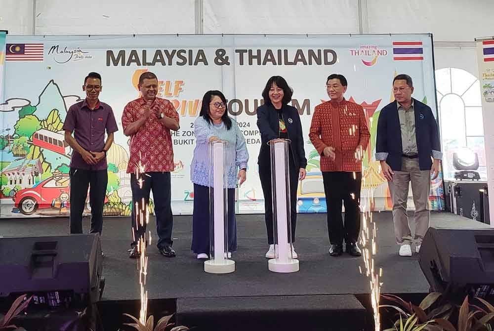 Dr Yasmeen (tiga kiri) dan Pattaraanong (tiga kanan) melakukan gimik pelancaran Malaysia-Thailand Self-Drive Tourism di lot parkir Kompleks Bebas Cukai Bukit Kayu Hitam, di sini, pada Sabtu.