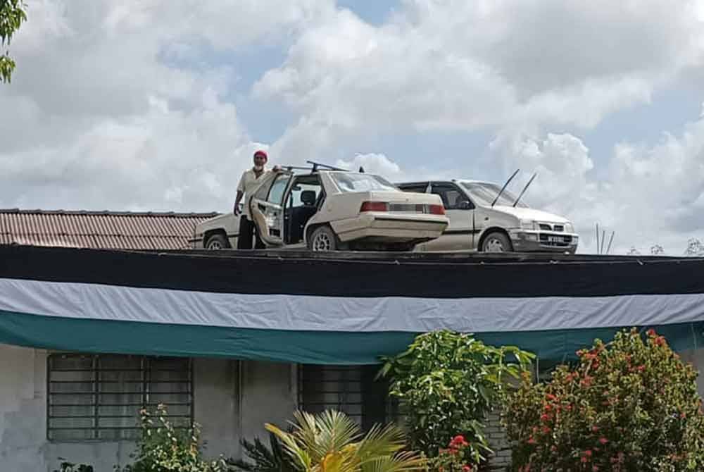 Awang Ali bersama dua keretanya yang diparkir buat sementara waktu di atas bumbung rumahnya di Kampung Matang Bonglai Kechil, Ayer Hitam.