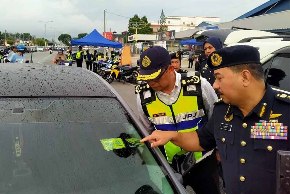 Muhammad Kifli (kanan) menunjukkan pelekat agensi penguat kuasa yang digunakan sebuah kenderaan ketika Ops Khas Motosikal 2024 di KM1 Jalan Sitiawan-Manjung di Manjung pada Isnin.