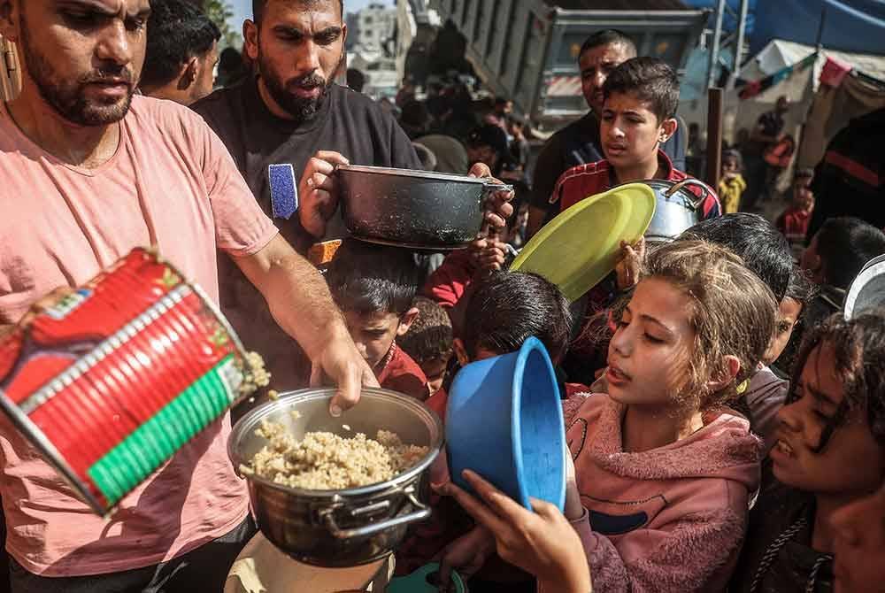 Sekumpulan kanak-kanak menunggu giliran untuk mendapatkan makanan yang diagihkan pekerja bantuan di tengah Gaza.