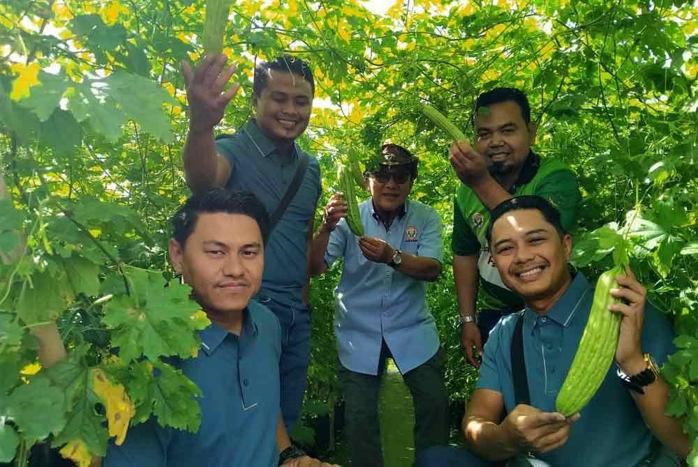 Khairul Faiez (berdiri, kiri), Hayadi Anuar (duduk, kanan) dan Shahizul (duduk, kiri) bersama Mohammed Akhiar (tengah) menunjukkan peria yang ditanam di ladangnya di Kampung Lasah di sini.