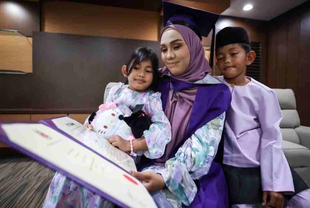 Ezuria Edora Dzafrul Akhtar, 30, menunjukkan Ijazah Sarjana Muda Pengurusan (Organisasi) kepada anaknya Ezriq Aisy Faiqal, 7, (kanan) dan Elise Arish Elliya, 5, pada Majlis Konvokesyen Universiti Sains Malaysia (USM) ke-62 pada Sabtu. Foto Bernama